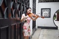 Beautiful Asian Chinese woman in traditional chi-pao cheongsam play violin in in a garden lean on a door Royalty Free Stock Photo