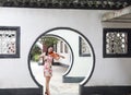 Beautiful Asian Chinese woman in traditional chi-pao cheongsam play violin in in a garden stand under arched door Royalty Free Stock Photo