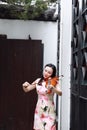 Beautiful Asian Chinese woman in traditional chi-pao cheongsam play violin in in a garden stand under arched door Royalty Free Stock Photo