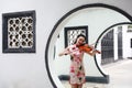 Beautiful Asian Chinese woman in traditional chi-pao cheongsam play violin in in a garden stand under arched door Royalty Free Stock Photo