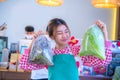 Beautiful asian farmer wearing an apron and holding a bag of fresh vegetables with both hands and smile on her face.