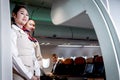 Beautiful Asian female air hostess standing at airplane entrance gate, flight attendant woman welcome and check passenger before