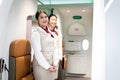 Beautiful Asian female air hostess standing at airplane entrance gate, flight attendant woman welcome and check passenger before