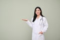 Beautiful Asian female doctor open palm, looking at camera, standing against grey background Royalty Free Stock Photo