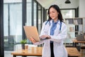 A beautiful Asian female doctor is using her laptop while standing in her office at a hospital Royalty Free Stock Photo