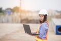 Beautiful Asian female engineer in white safety hard hat using laptop computer notebook doing job at construction site outside Royalty Free Stock Photo