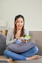 Beautiful Asian female enjoys eating her healthy and organic green salad on her couch Royalty Free Stock Photo