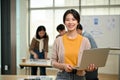 A beautiful Asian female graphic designer stands in the co-working office with a laptop in her hand Royalty Free Stock Photo