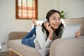 Beautiful Asian female with headphones, watching movie through her tablet while lying on sofa Royalty Free Stock Photo
