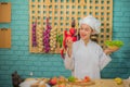 Beautiful asian female professional chef holding and looking to an apple and bowl of fresh green vegetables in the kitchen. Royalty Free Stock Photo