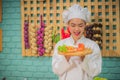 Beautiful asian female professional chef holding and looking to a wooden tray with tomatoes fresh green vegetables and bread in Royalty Free Stock Photo