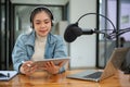 A beautiful Asian female radio host is looking at her tablet screen, speaking into a microphone Royalty Free Stock Photo