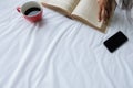 Beautiful asian female sitting on the bed with a cup of coffee and reading a book