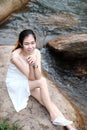 Beautiful asian female in white dress is hand holding grass flower on the rock and stream in forest Royalty Free Stock Photo