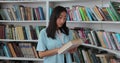 Beautiful asian girl in blue shirt walks along the shelves with books in the library. College education concept. Royalty Free Stock Photo