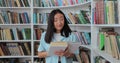 Beautiful asian girl in blue shirt walks along the shelves with books in the library. College education concept. Royalty Free Stock Photo
