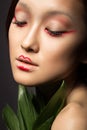 Beautiful Asian girl with a bright make-up art in green leaves. Beauty face. Creative image.