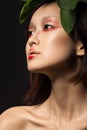 Beautiful Asian girl with a bright make-up art in green leaves. Beauty face. Creative image.