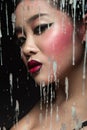 Beautiful Asian girl with bright make-up behind glass and drops of wax. Beauty face. Royalty Free Stock Photo