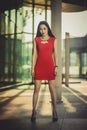 Beautiful Asian girl model in red dress posing at the modern glass style city background. Sunny day. Royalty Free Stock Photo