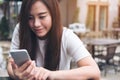Asian girl with smiley face holding and using smart phone in modern cafe Royalty Free Stock Photo