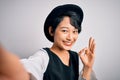 Beautiful asian girl wearing casual hat making selfie by the camera over white background doing ok sign with fingers, excellent Royalty Free Stock Photo