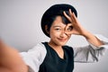 Beautiful asian girl wearing casual hat making selfie by the camera over white background with happy face smiling doing ok sign Royalty Free Stock Photo