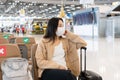 Beautiful Asian girl wearing medical mask sitting at international airport while waiting for check in counter open.