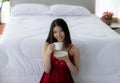 Beautiful Asian girl. Wearing red pajamas sitting in the white bedroom. Listening to music. On the morning she sitting and Royalty Free Stock Photo