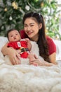 Beautiful Asian mom woman wear red cloth hugging newborn baby in christmas theme at cozy home.Happy infant baby looking at camera Royalty Free Stock Photo