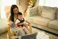 Beautiful Asian mother with baby son working on laptop at home Royalty Free Stock Photo