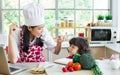 Beautiful Asian mother cooking for breakfast while taking care her mixed race adorable little daughter to do homework, online Royalty Free Stock Photo