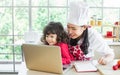 Beautiful Asian mother cooking for breakfast while taking care her mixed race adorable little daughter to do homework, online Royalty Free Stock Photo