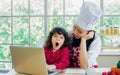 Beautiful Asian mother cooking for breakfast while taking care her mixed race adorable little daughter to do homework, online Royalty Free Stock Photo