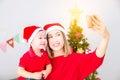 Asian mother with her son wearing christmas costume and taking photo themself by smartphone at home with christmas