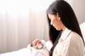 Beautiful Asian mother is holding and look at her newborn baby with love in front of white curtain with day light Royalty Free Stock Photo