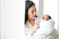 Beautiful Asian mother look to her newborn baby yawn in front of white curtain with day light