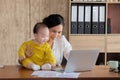 Beautiful Asian mother spent time with curiosity toddler baby boy talking, playing on workplace home, adorable naughty son happy Royalty Free Stock Photo