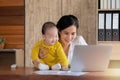 Beautiful Asian mother spent time with curiosity toddler baby boy talking, playing on workplace home, adorable naughty son happy Royalty Free Stock Photo