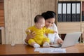 Beautiful Asian mother spent time with curiosity toddler baby talking, playing at workplace home, adorable naughty son happy Royalty Free Stock Photo