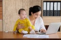 Beautiful Asian mother spent time with curiosity toddler baby talking, playing at workplace home, adorable naughty son happy Royalty Free Stock Photo