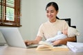 A beautiful Asian mother working at home and holding her baby in her arms Royalty Free Stock Photo