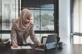 Beautiful asian muslim business woman brown hijab sitting and working with laptop computer at modern office