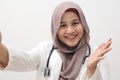 Beautiful Asian muslim female doctor wearing hijab and suit taking selfie photo. Medical doctor doing video call, smiling and Royalty Free Stock Photo