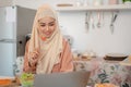 A beautiful Asian Muslim woman is eating her salad bowl while working on her laptop Royalty Free Stock Photo
