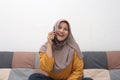 Beautiful Asian muslim woman using phone while sitting on sofa, girl talking on smartphone and smiling Royalty Free Stock Photo