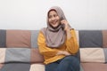 Beautiful Asian muslim woman using phone while sitting on sofa, girl talking on smartphone and smiling Royalty Free Stock Photo