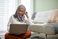 Beautiful Asian Muslim woman wearing hijab using laptop and sitting in her living room Royalty Free Stock Photo