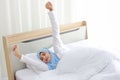 Beautiful asian muslim woman wearing white sleepwear lying on bed, stretching her arms after getting up in the morning at sunrise Royalty Free Stock Photo