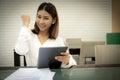 Beautiful asian office girl wearing white dress is sitting showing fist while holding tablet with smile on her face, Business Royalty Free Stock Photo